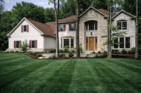A white stucco and stone two-story custom home with red shutters built by Sudon Brothers